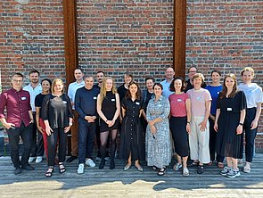 Gruppe der Teilnehmenden des ersten Workshops zum Thema Circular steht in einer Reihe vor einer Backsteinwand im Freien