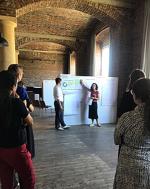 Gruppe der Teilnehmenden des ersten Circular-Workshops in einem Raum , zwei Personen präsentieren mit einem großen Poster Diagramme